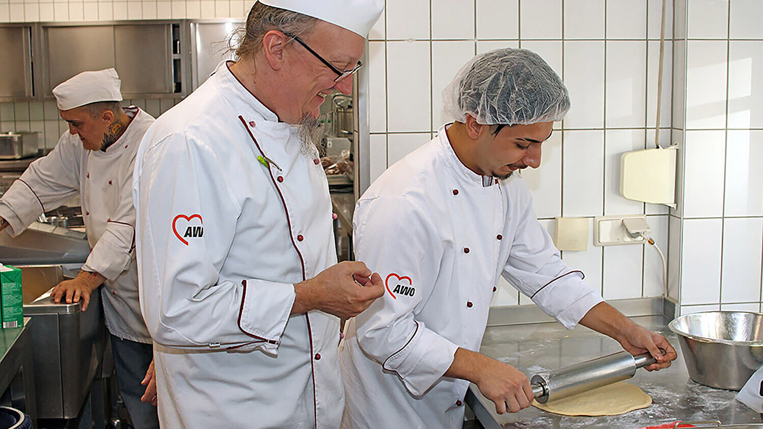 AWO_Ludwigsburg_Hans-Klenk-Haus_Kochen.jpg In der Küche des Hans-Klenk-Haus wird ausgebildet: Geert Seifert zeigt Ibrahim Caliskan, wie der Teig für Zwiebelkuchen ausgerollt wird
