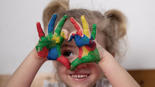Ein Kita-Kind streckt seine bunten, mit Farbe verschmierten Hände in die Kamera